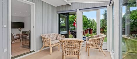 A sunlit room with wicker furniture, a television, and a view of a red building outside.