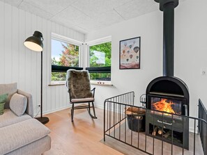 Ein gemütliches Wohnzimmer mit Kamin, einem bequemen Sessel, einer Couch und einem großen Fenster mit Blick auf Grünflächen.