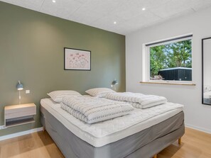 Ein modernes Schlafzimmer mit Bett, Nachttischen, einem Fenster und einem gerahmten Bild an der Wand.