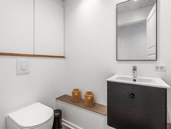 A modern bathroom with a white toilet, a dark vanity, a mirror, and two decorative baskets on a shelf.