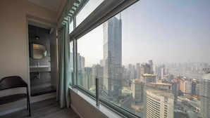 A room with a large window, a chair, a mirror, and a view of a cityscape with tall buildings. - Style INS High-Altitude River View Hotel (Chongqing)