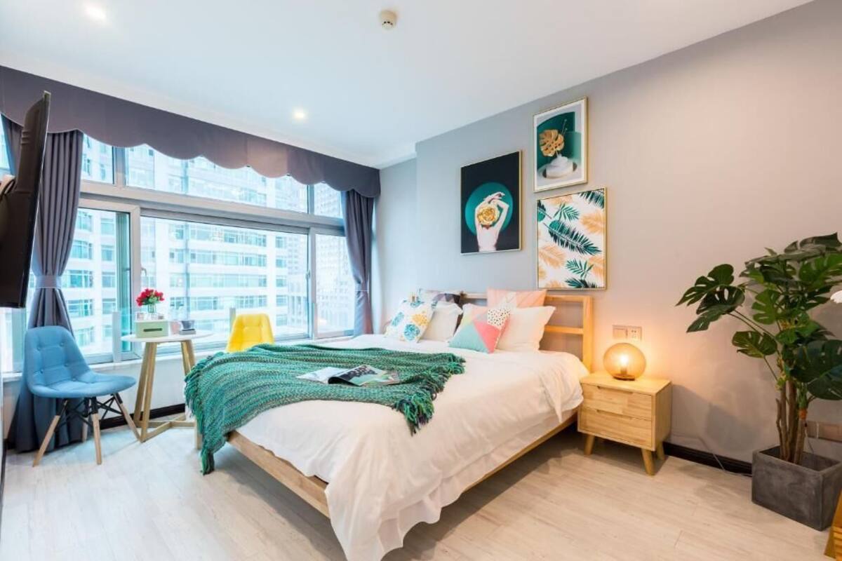 A modern bedroom with a bed, bedside table, chair, and large window.