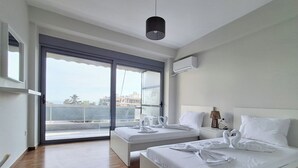 A modern hotel room with a large bed, a smaller bed, a balcony, and a view of the city. - Elegant Apt at Alimos Marina Sea View (Alimos)