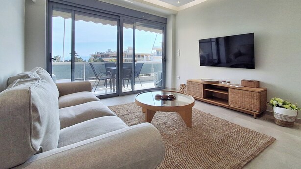 A modern living room with a sofa, a coffee table, a TV, and a balcony with a view. - Elegant Apt at Alimos Marina Sea View (Alimos)