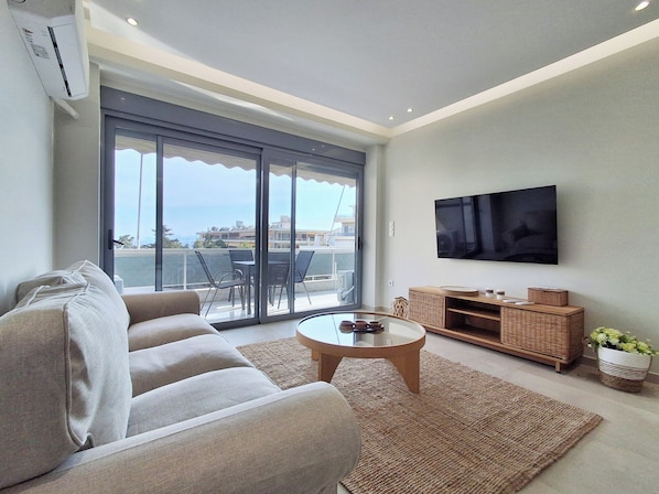 A modern living room with a sofa, a coffee table, a TV, and a balcony with a view. - Elegant Apt at Alimos Marina Sea View (Alimos)
