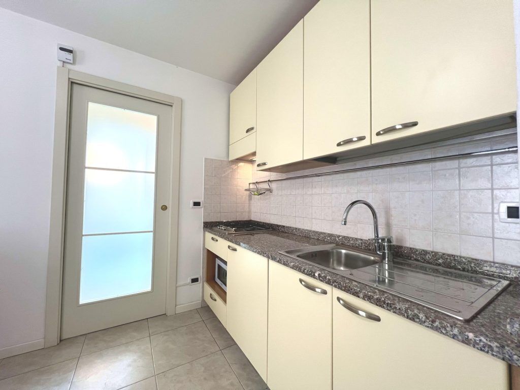 A kitchen with white cabinets, a granite countertop, a stainless steel sink, and a frosted glass door.