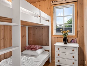 Une chambre avec un lit superposé, une fenêtre, des murs en bois et une commode avec des tiroirs.