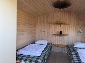 Ein Zimmer mit Holzboden, zwei Betten, einem Regal mit einer Vase und einem Deckenventilator.