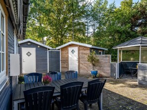 Un espace patio avec une table et des chaises en bois, entouré d’une clôture en bois et comprenant un coin salon abrité.