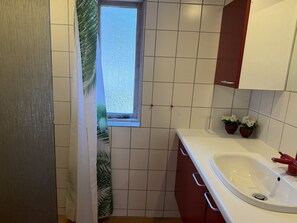 Ein Badezimmer mit weißen Fliesen, einem Fenster, einem Waschbecken und roten Schränken.