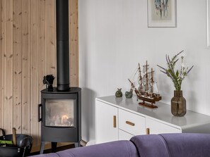 Une pièce avec un poêle à bois, un meuble contenant des objets décoratifs et un canapé violet.
