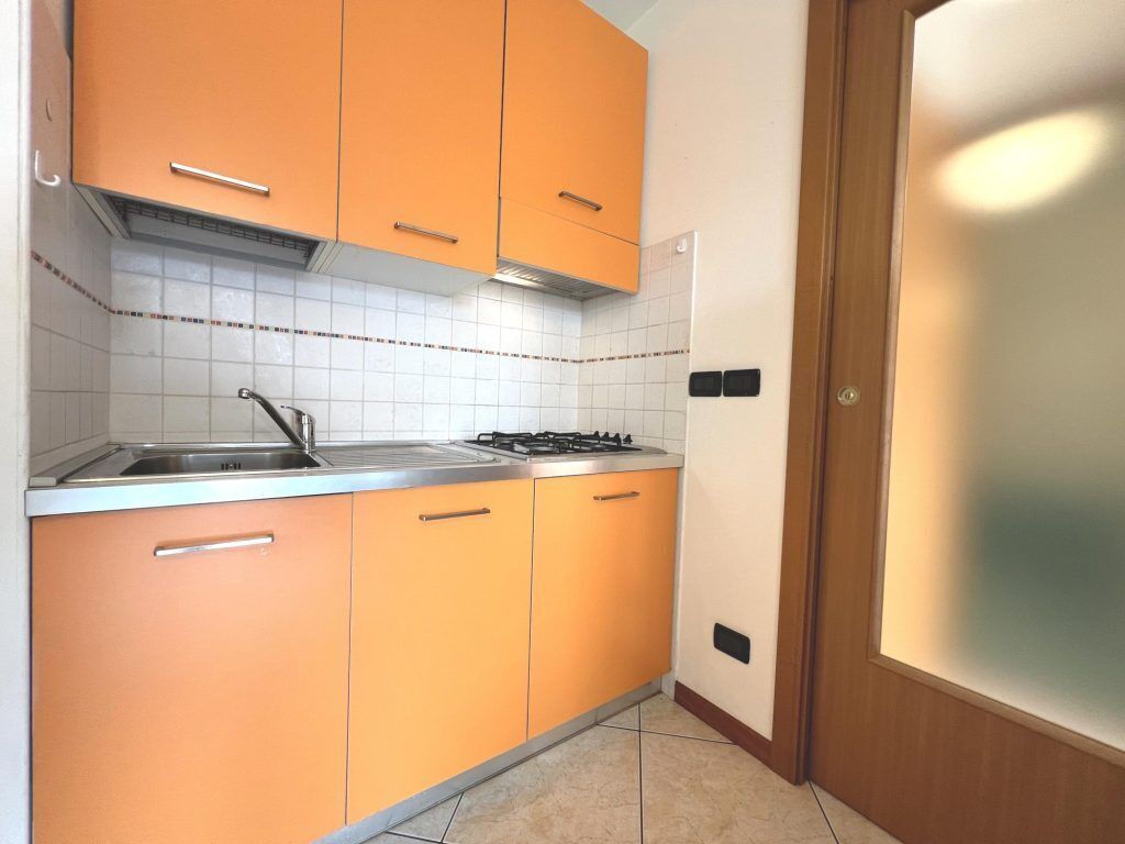 Una cocina con armarios color naranja, un lavamanos de acero inoxidable y una estufa a gas.