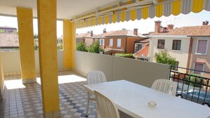 En balkon med gulv i skakmønster, et hvidt bord og stole, samt en markise med gule striber.