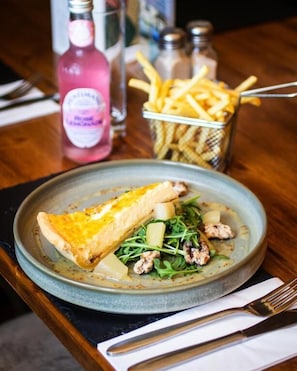 A plate of food with a slice of pie, fries, and greens on a table with a bottle and salt shakers in the background. - The White Hart Inn  (Ingatestone)