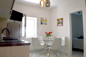 Eine moderne Küche mit Flachbildfernseher, weißen Stühlen, einem Glastisch und Bildern an den Wänden.
