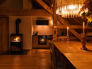 A cozy room with a wood-burning stove, a dining table with candles, and a television mounted on the wall. - Villa Senz - Happiness (Pfronten)