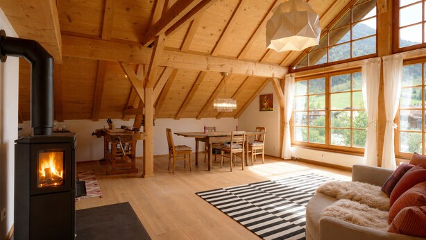 Un interior de madera con estufa de leña, zona de comedor y ventanas amplias.