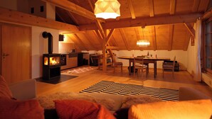 Una habitación acogedora en el ático con techo de madera, chimenea, una mesa de comedor y un sofá.