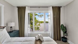 Een hotelkamer met een bed, nachtkastje, lamp, raam met gordijnen en een bloempot.