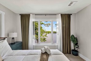 Ein Hotelzimmer mit einem Bett, einem Nachttisch, einer Lampe, einem Fenster mit Vorhängen und einer Zimmerpflanze.