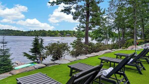 Een terras aan het meer met lounge fauteuils, een klein bootje en uitzicht op het meer en bos.