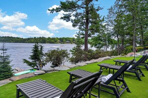 Eine Seeterrasse mit Liegestühlen, einem kleinen Boot und Blick auf See und Wald.