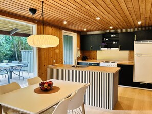 Eine moderne Küche mit Holzbalkendecke, ein Essbereich mit Tisch und Stühlen sowie Blick ins Freie.