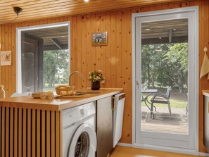 Eine kompakte Küche mit integriertem Waschmaschine, Holzwänden, einem großen Fenster und Blick auf eine Terrasses.