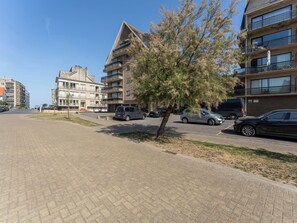 Ein Mehrfamilienhaus mit mehreren Etagen, Balkonen und einem Parkplatz mit Autos.