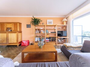 Ein Wohnzimmer mit Couch, Fernseher, Bücherregal und einem Holztisch.