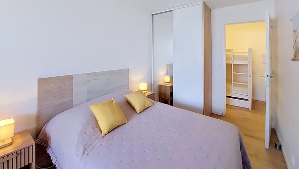 Ein Schlafzimmer mit einem Bett, Nachttischlampen, einem Kleiderschrank und einem Spiegel.