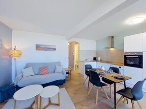 A compact living space with a sofa, dining table, chairs, a lamp, and a kitchen area. - Résidence du Port by Interhome (Arcachon)