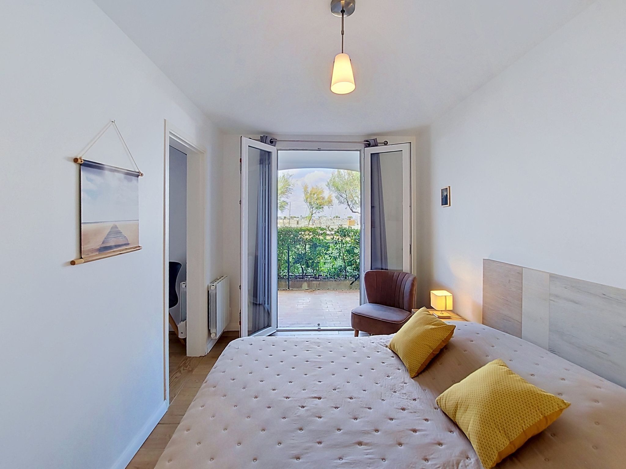 A bedroom with a bed, a chair, a lamp, and a view of the outdoors.