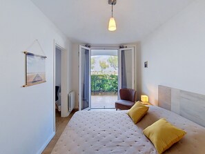 A bedroom with a bed, a chair, a lamp, and a view of the outdoors. - Résidence du Port by Interhome (Arcachon)