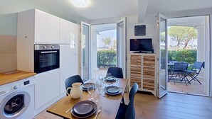 Eine kompakte Küche mit modernen Geräten, ein Essbereich mit Tisch für zwei Personen und ein an einem Holzkasten montierter Fernseher.