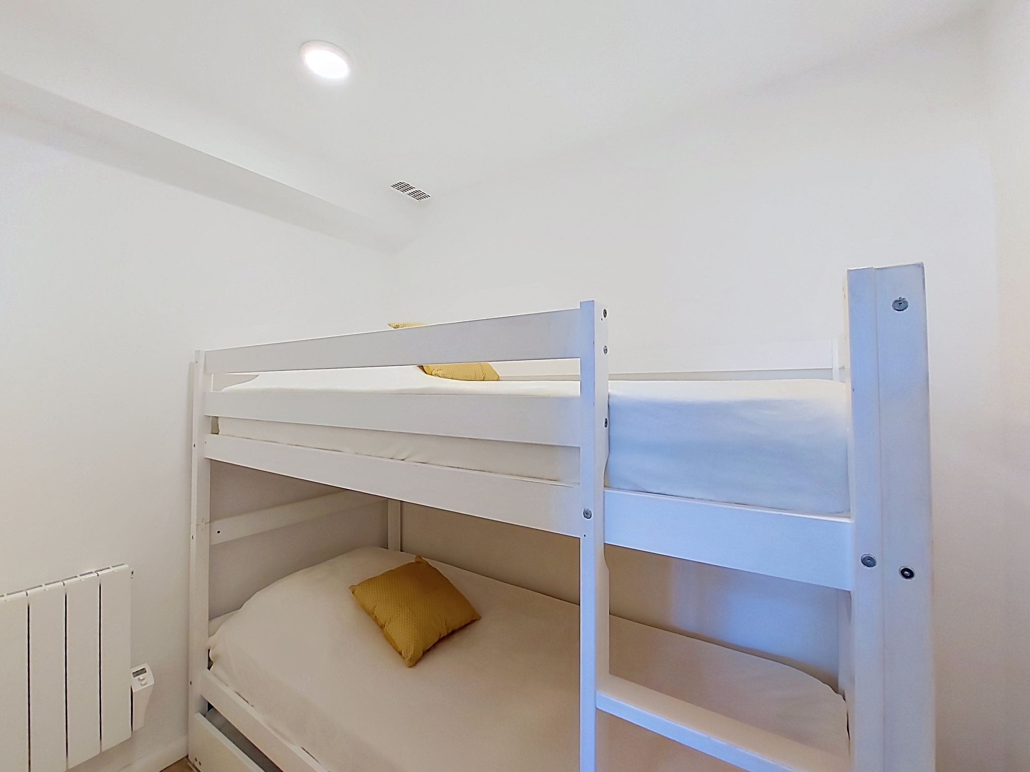 A bunk bed with a mattress and a pillow, a radiator, and a ceiling light.