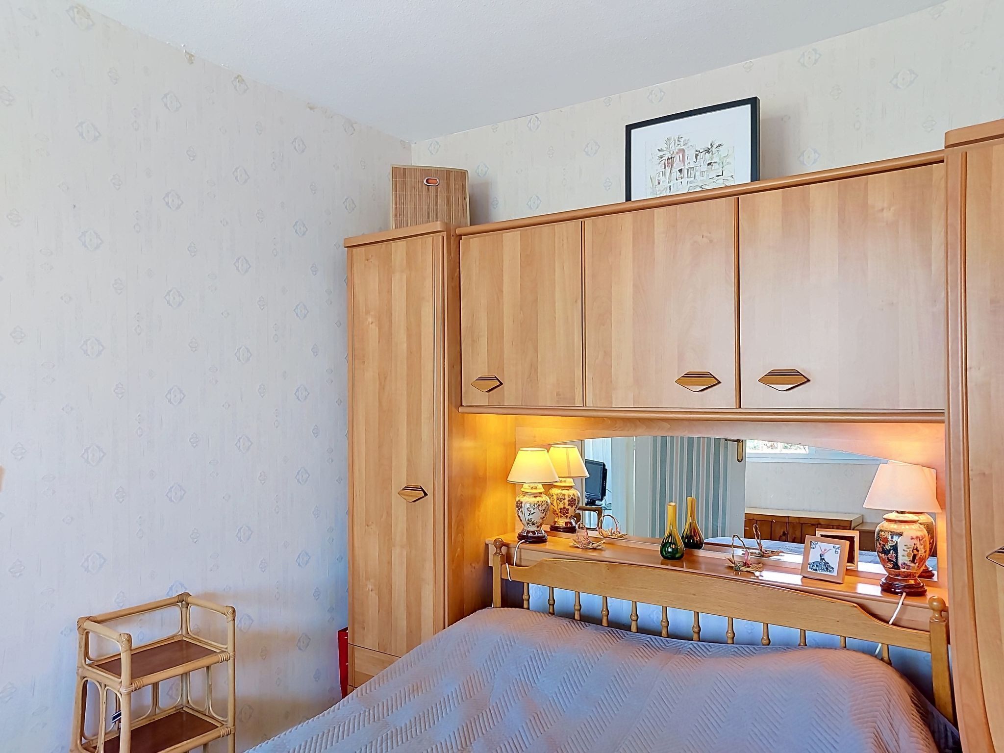 Een slaapkamer met een houten garderobe, een bed met hoofdeinde, een nachtkastje met lampen en een klein houten krukje.