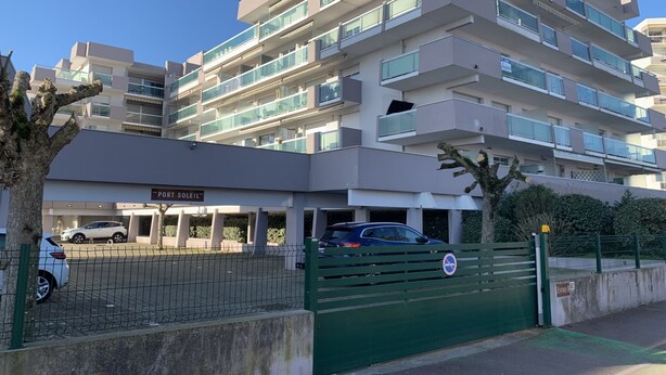 Een meerlaags woongebouw met balkons, een parkeerplaats en een poort.