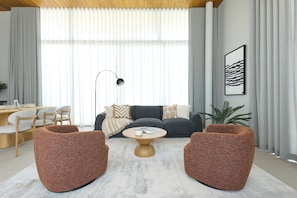 Een moderne woonkamer met een bank, twee fauteuils, een salontafel en een eethoek met stoelen en een tafel.