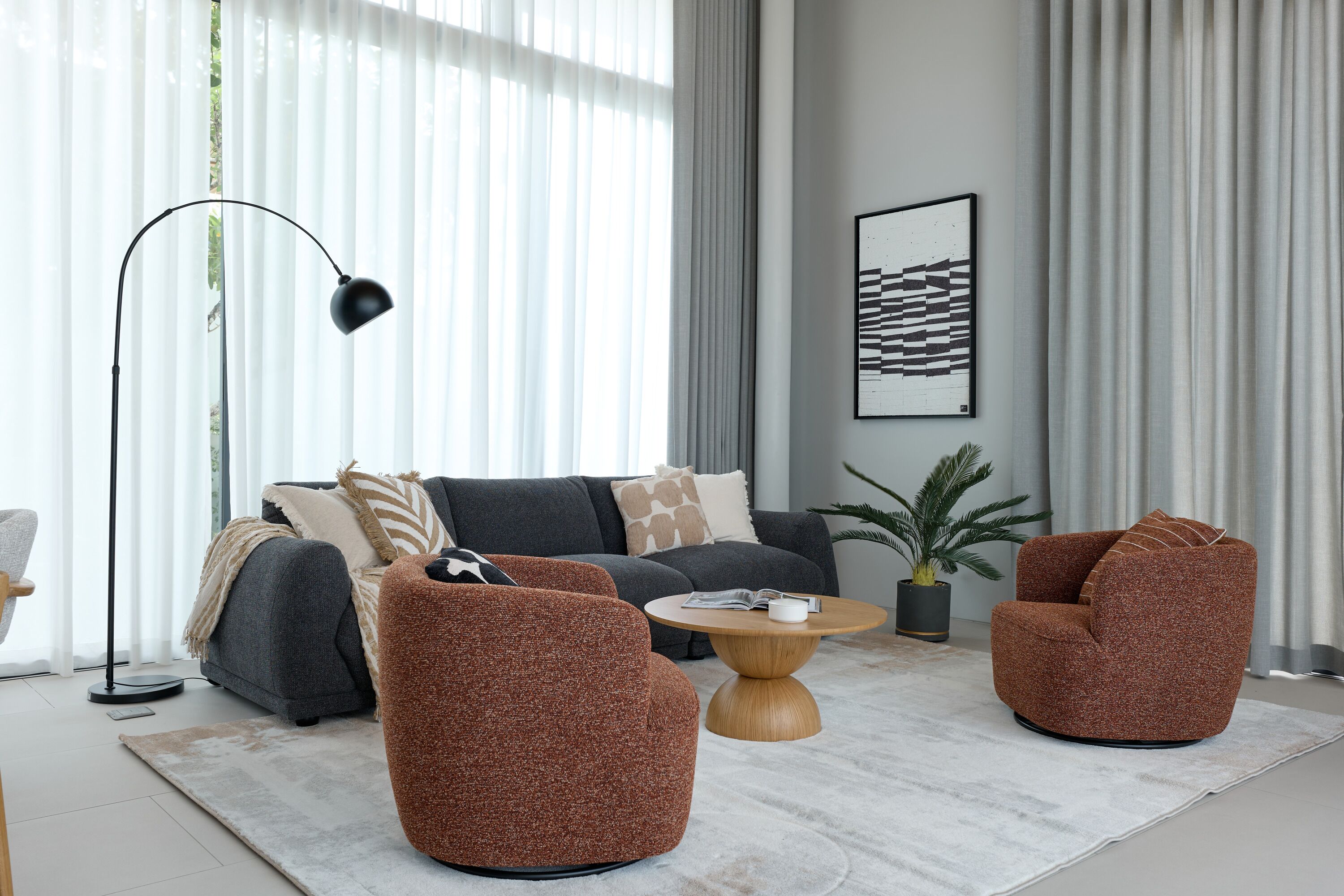 A modern living room with a grey sofa, two brown armchairs, a coffee table, a floor lamp, and a potted plant.