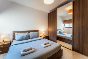 A hotel room with a large bed, bedside tables, a mirror, and a window.
