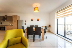 A modern kitchen with a dining area, a yellow armchair, and a large window.