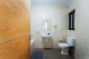 A bathroom with a wooden door, a sink, a toilet, and a mirror. - Coastal Sea View Escape with Sunset Balcony (Mellieha)