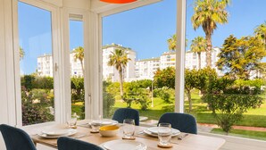 Uma sala de jantar com mesa posta para quatro pessoas, janelas amplas com vista para edifícios e áreas verdes.