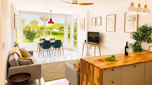 Cozinha moderna com ilha de madeira, área de refeições com cadeiras, uma TV e obras de arte nas paredes.