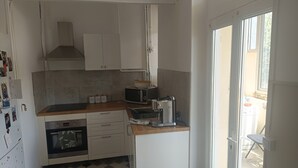 Eine kompakte Küche mit weißen Schränken, einer Mikrowelle, einer Kaffeemaschine und einem kleinen Backofen.