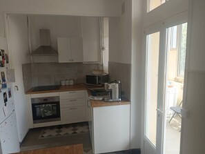 Cocina compacta con armarios blancos, microondas, cafetera y horno pequeño.