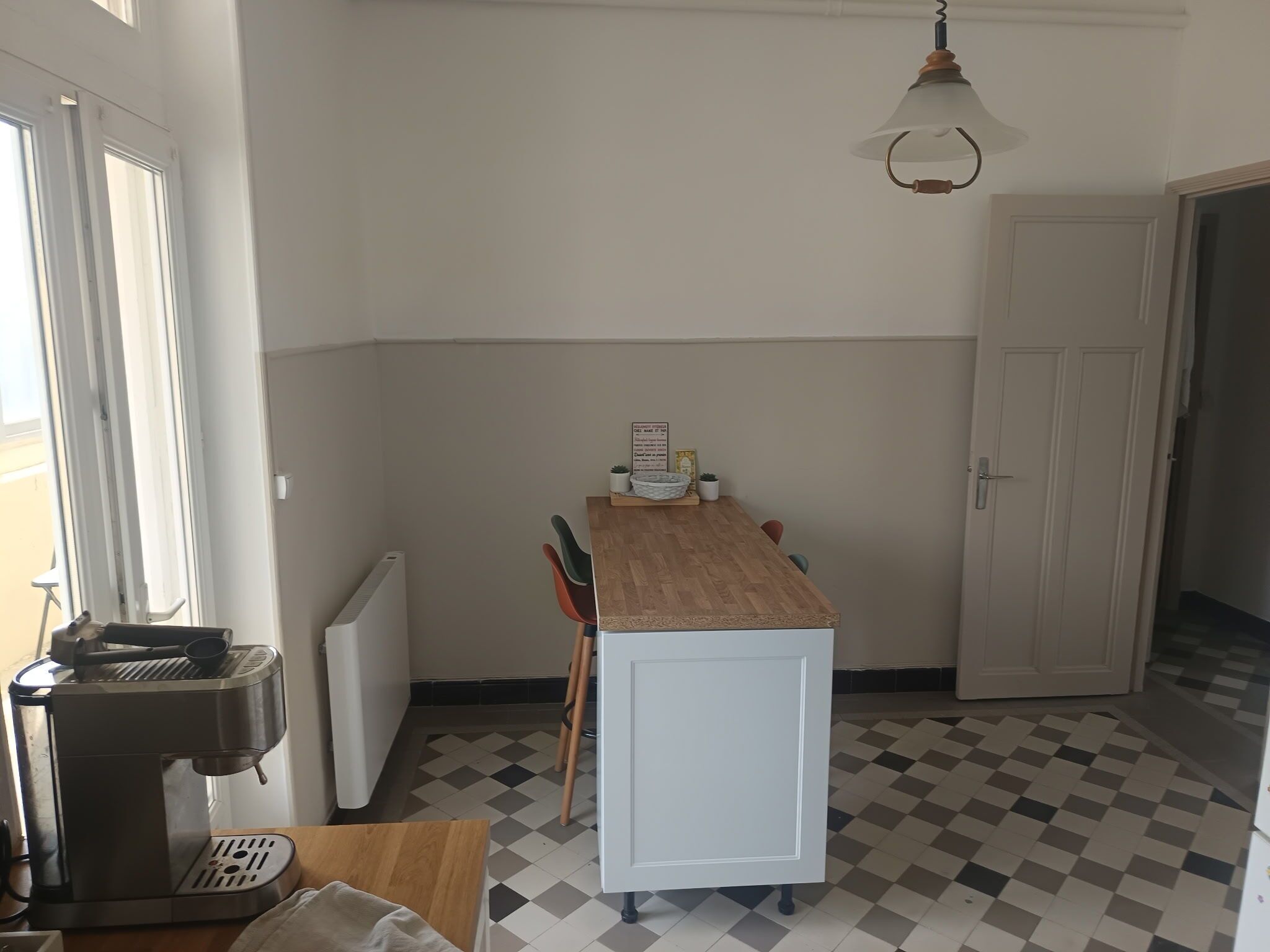 Una pequeña cocina con cafetera, radiador, suelo a cuadros y una puerta.
