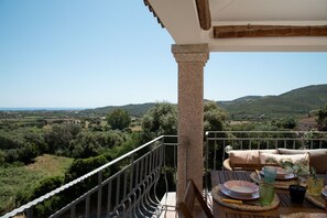 Un balcon donnant sur un paysage vallonné, une table dressée avec des assiettes, des verres et une plante.