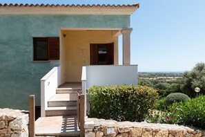 A two-story house with a stone staircase leading to a wooden door, a stone wall, and a view of the countryside. - Casa Luna e Sole by Wonderful Italy (Budoni)